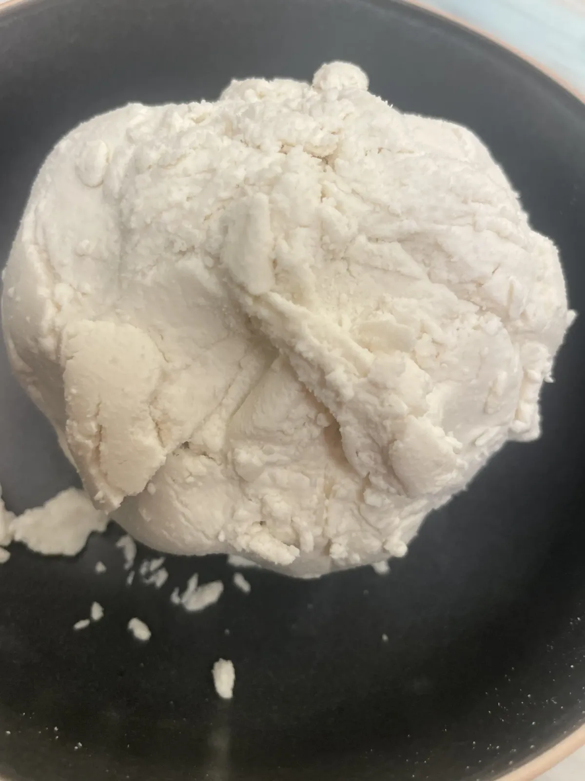 A mound of fluffy homemade white vegan almond ricotta on a matte black ceramic dish