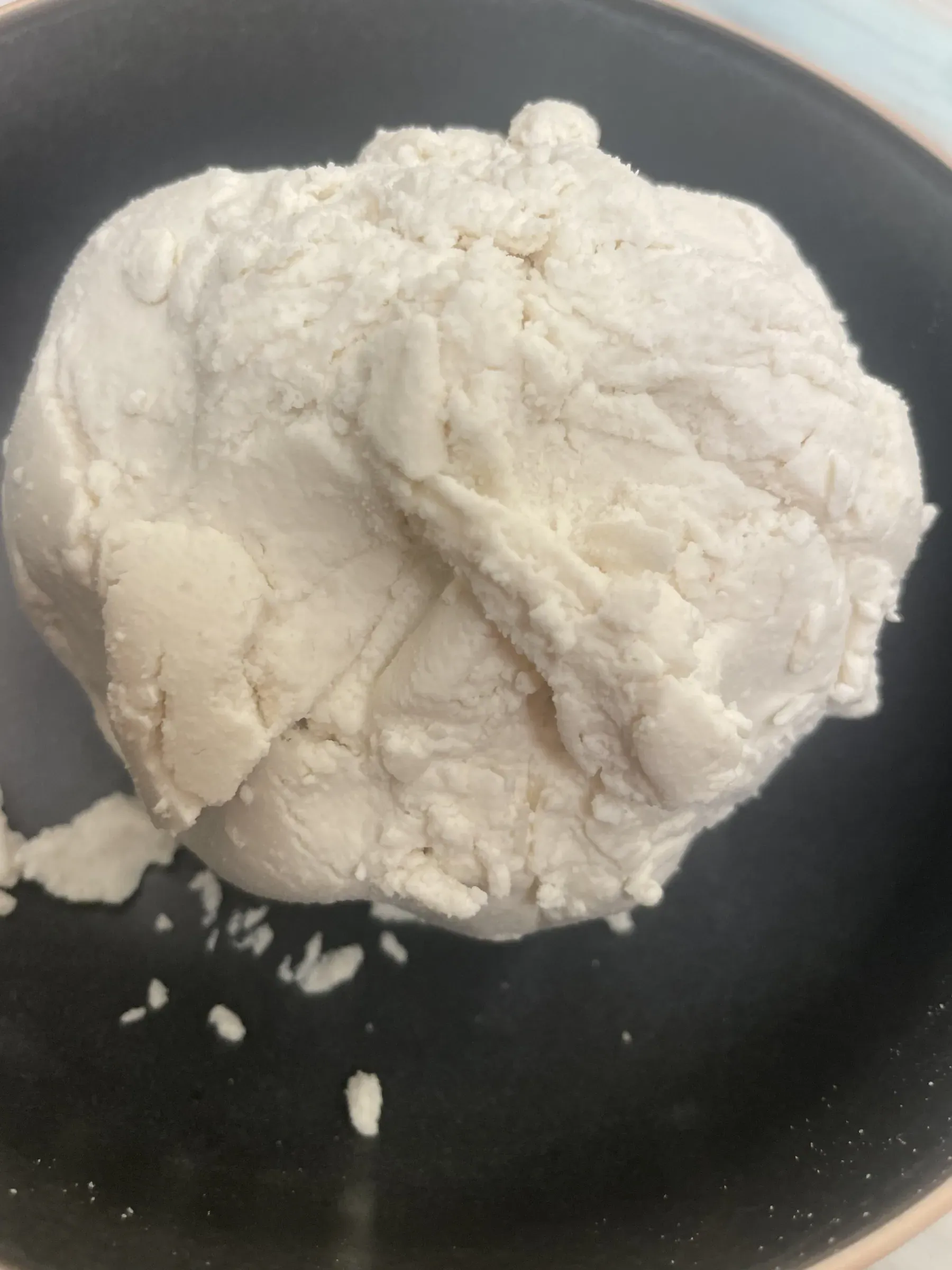 A mound of fluffy homemade white vegan almond ricotta on a matte black ceramic dish