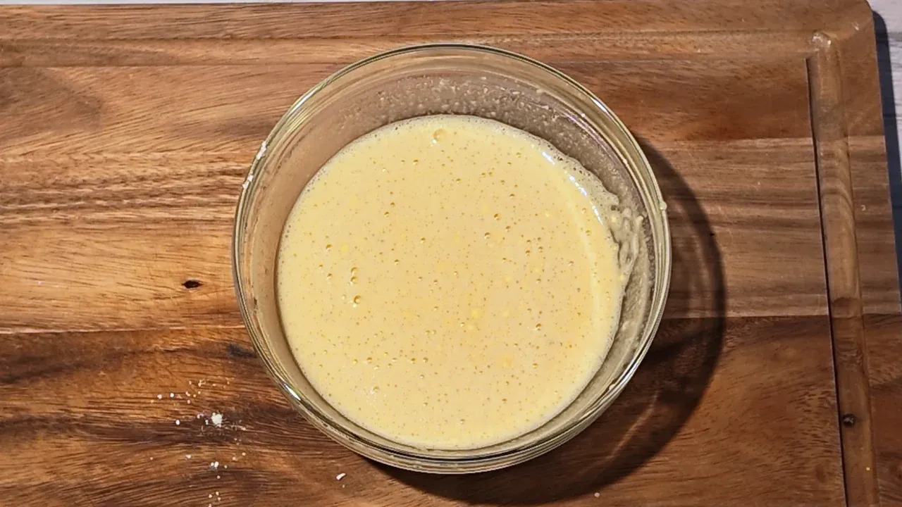 Overhead view of freshly whisked chickpea batter in a glass bowl on a wooden board