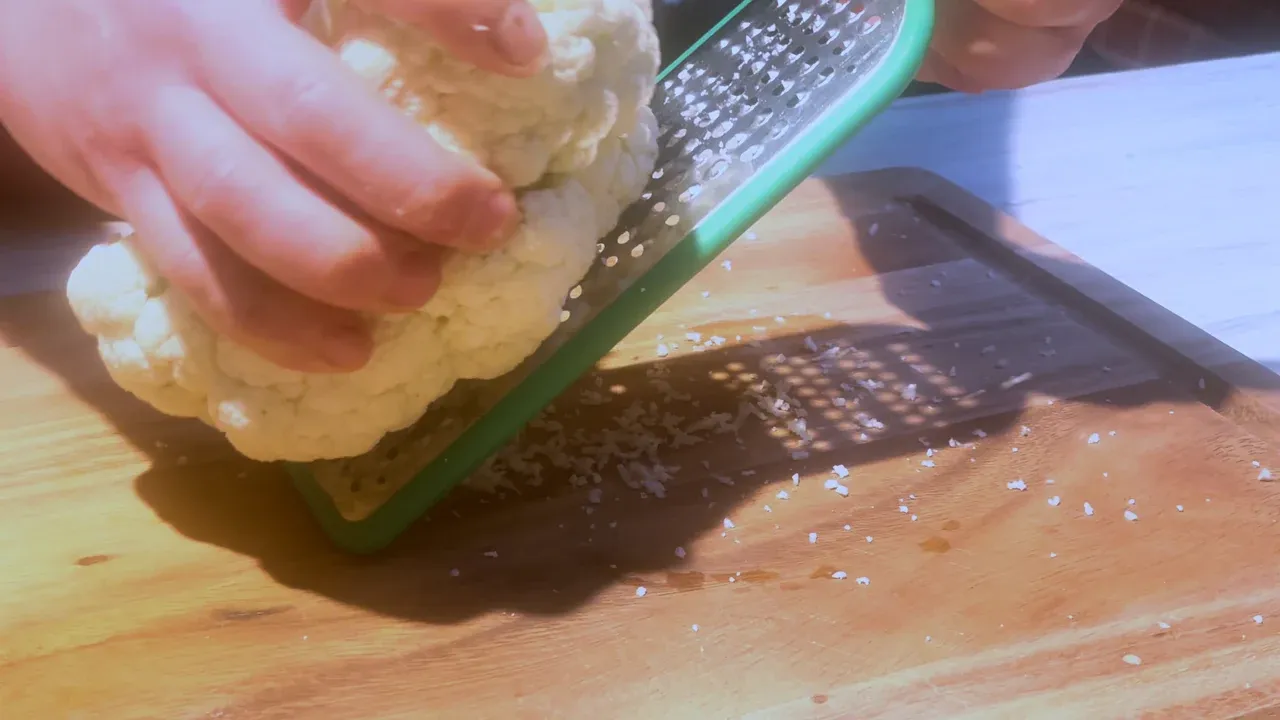 Raw cauliflower rubbed on a flat green grater over a wooden board