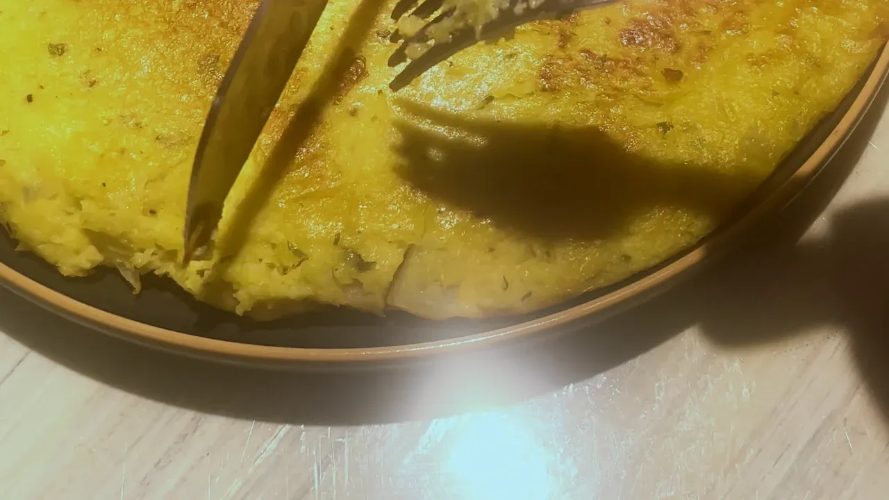 A knife cutting the golden omelette into wedges on a plate, a fork holding it