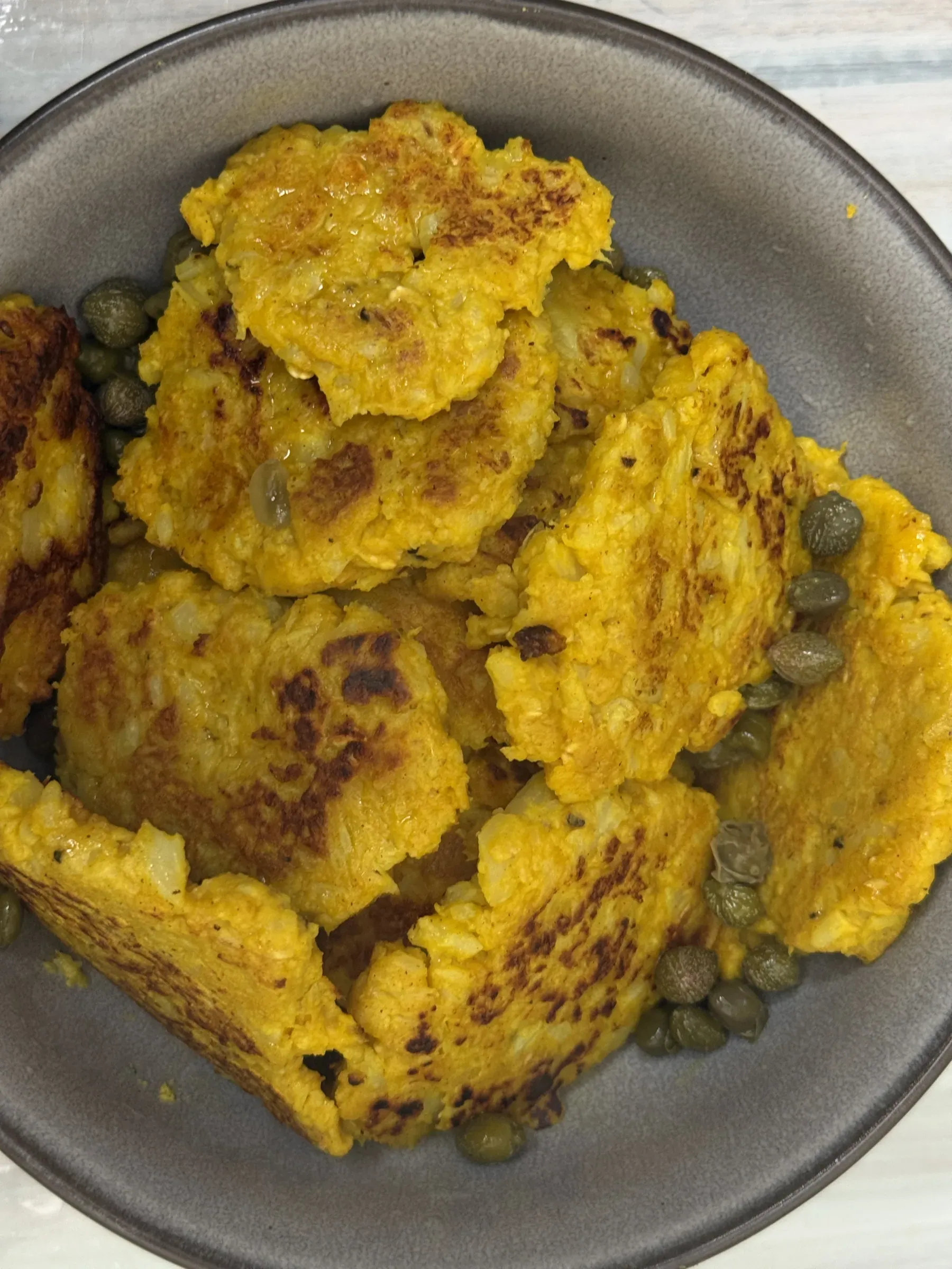 Crispy pan-fried cauliflower fritters piled in a bowl and garnished with green capers