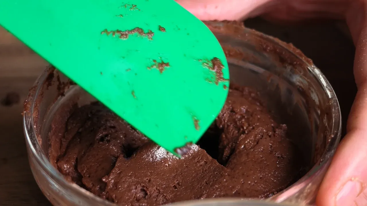 A green spatula smoothing chocolate batter over the hidden chocolate square