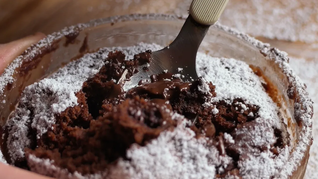A teaspoon opening the molten chocolate centre of the cake under a layer of icing sugar