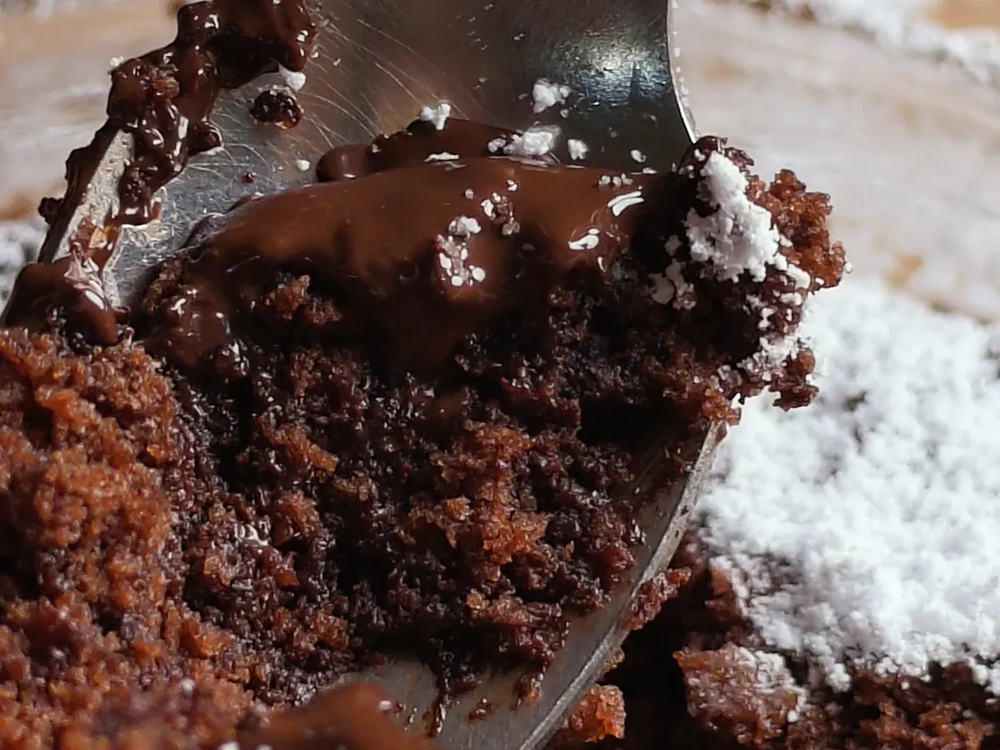 Close-up of a teaspoon lifting soft chocolate cake and molten dark chocolate out of a bowl dusted with icing sugar