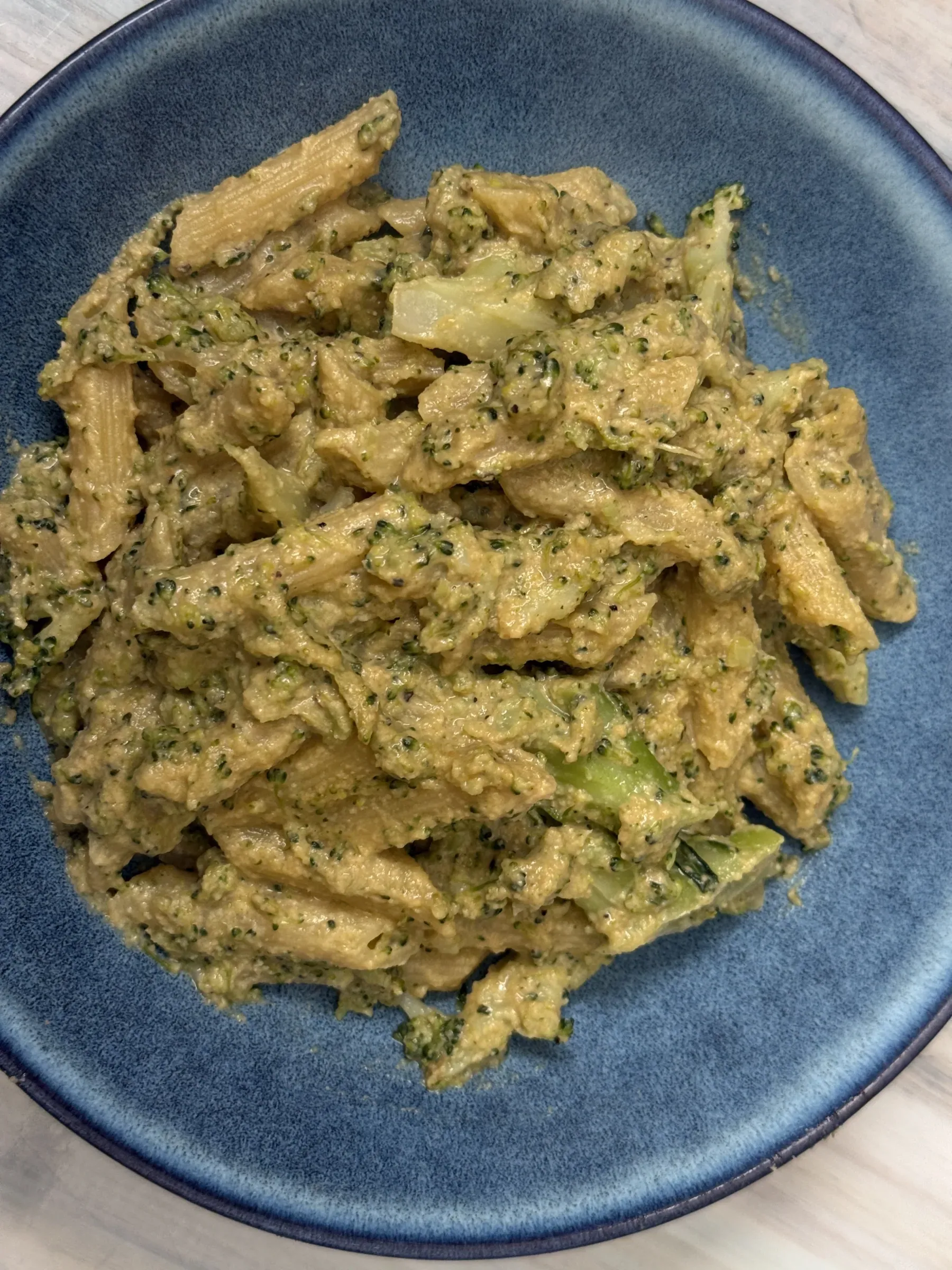 A steaming bowl of creamy vegan broccoli penne pasta with a rich green cashew cream sauce
