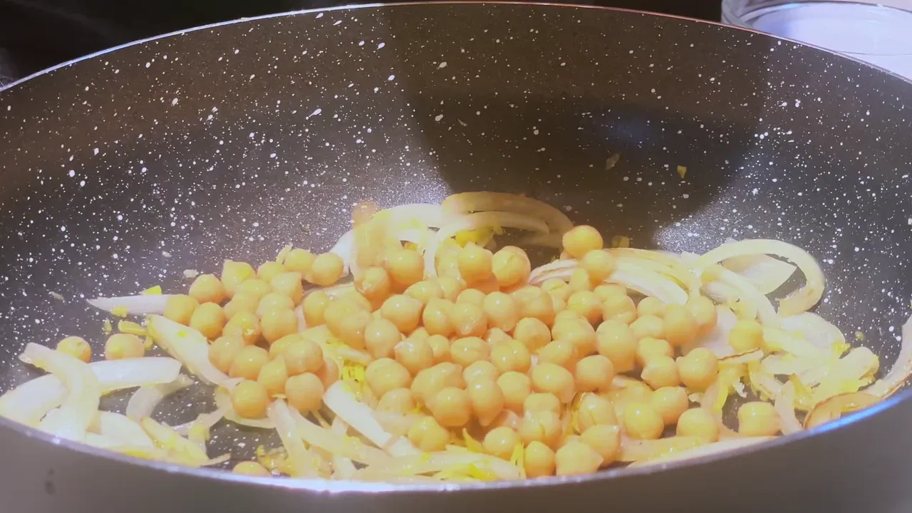 Chickpeas just tipped onto softened onion slices and lemon zest in a speckled non-stick pan