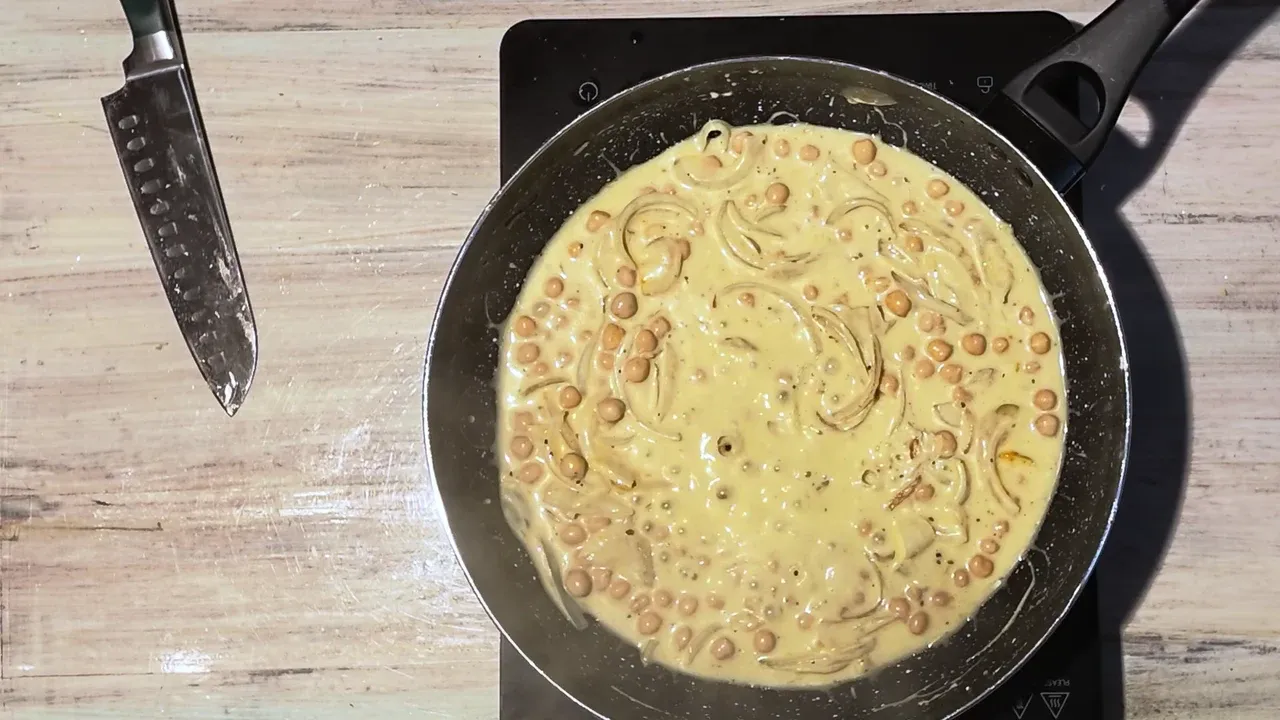 Thick, creamy coconut sauce with chickpeas and onion in a black pan, seen from above