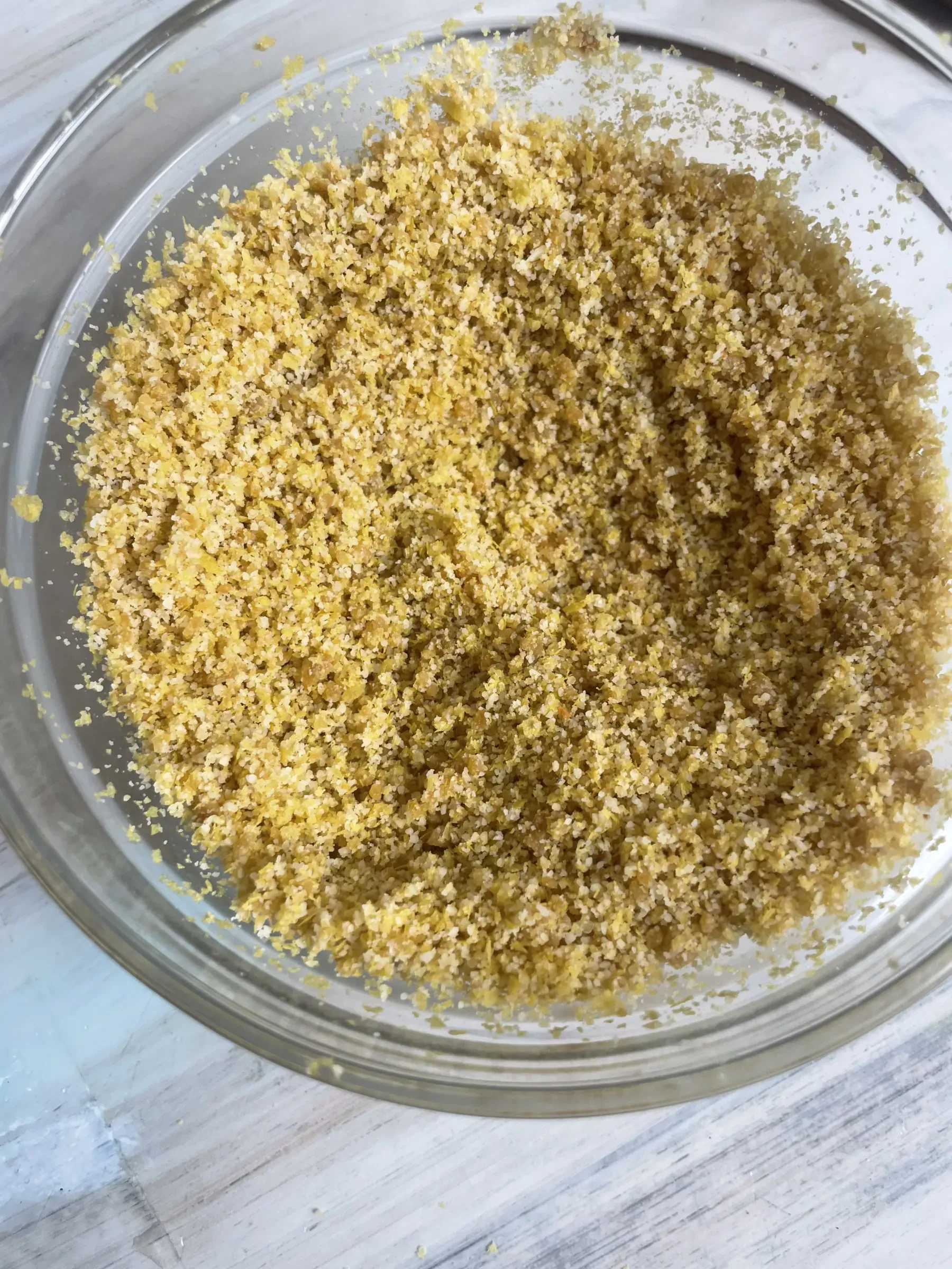 A clear glass bowl containing golden vegan parmesan cheese crumbs
