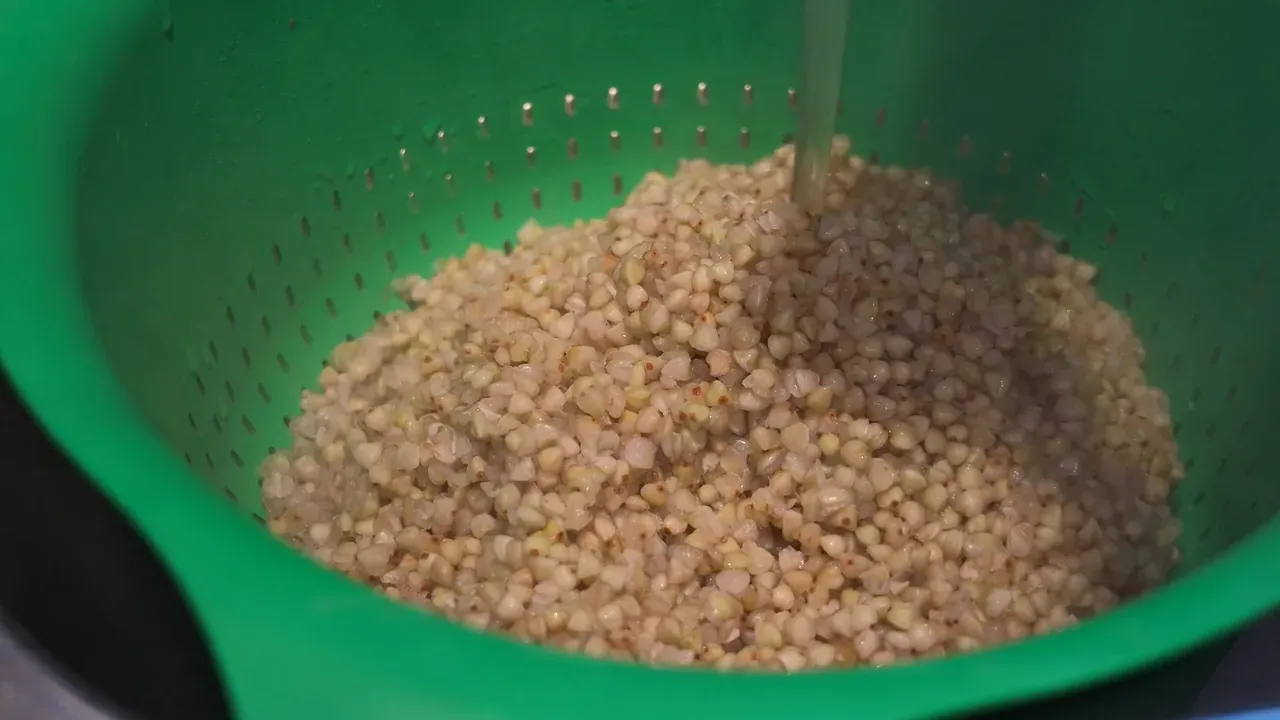 Tap water running onto cooked buckwheat in a green colander
