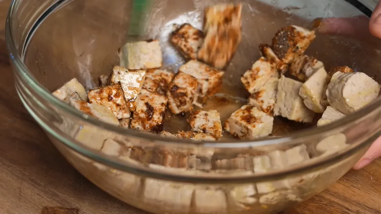 Tempeh cubes coated in smoked paprika and spices, tossed with a green spatula in a glass bowl