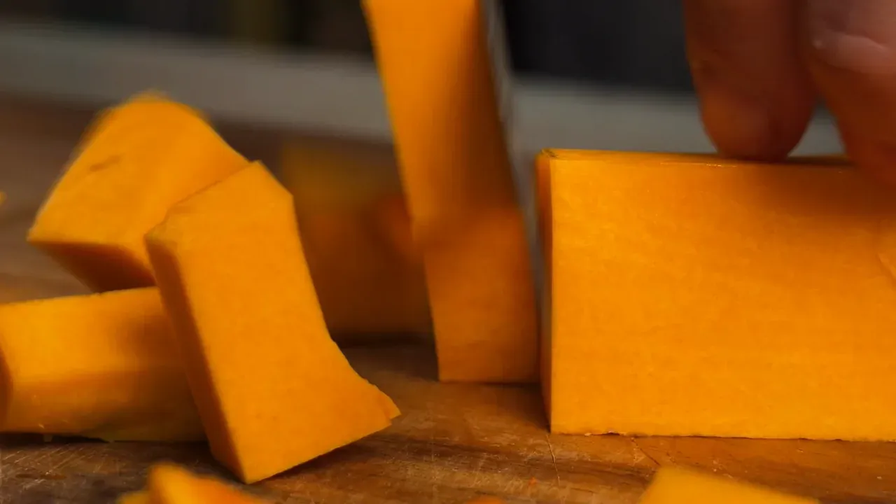 Peeled orange pumpkin cut into cubes on a wooden board