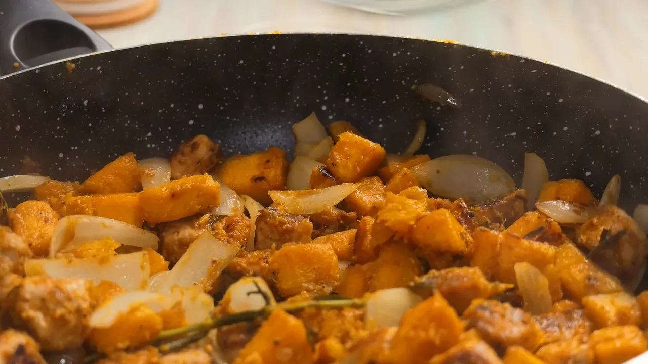 Close-up of onion petals cooking with golden pumpkin and tempeh in the pan