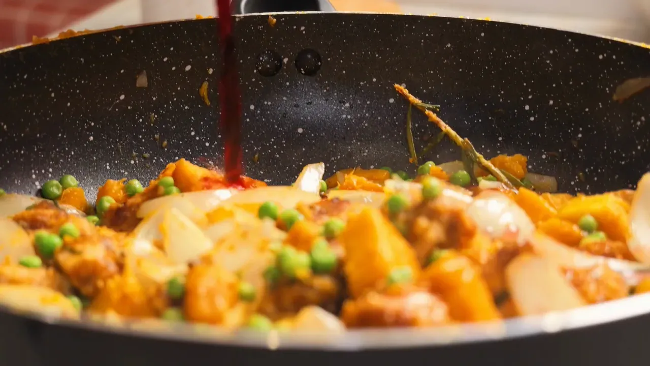 Red wine poured over tempeh, pumpkin, onion and green peas in the pan