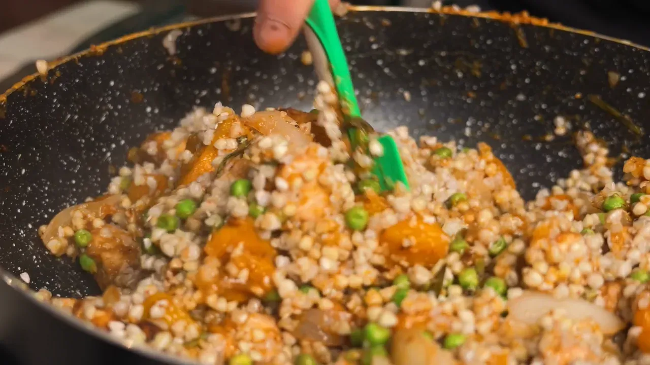 Buckwheat mixed with pumpkin, tempeh, onion and peas in the pan, stirred with a green spatula
