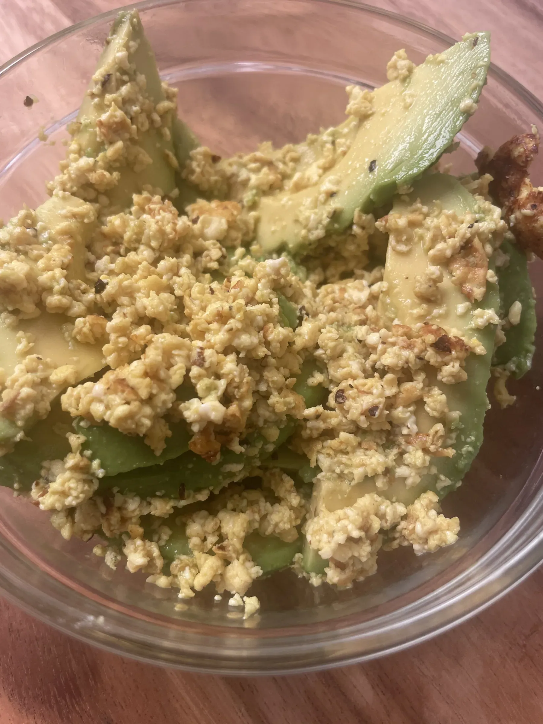 A bowl of golden scrambled vegan tofu curds served with fresh sliced avocado