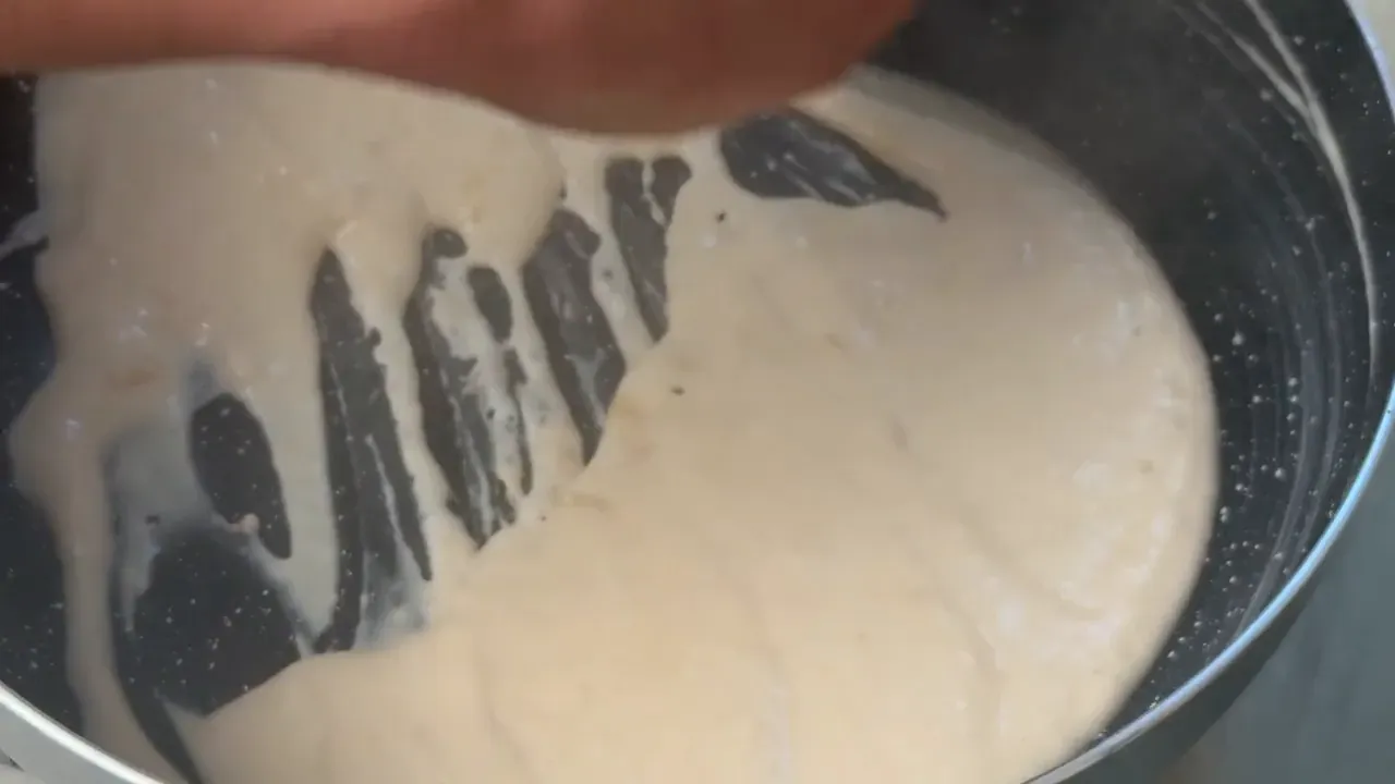 Thick, glossy vegan cheese being stirred in a dark non-stick pan