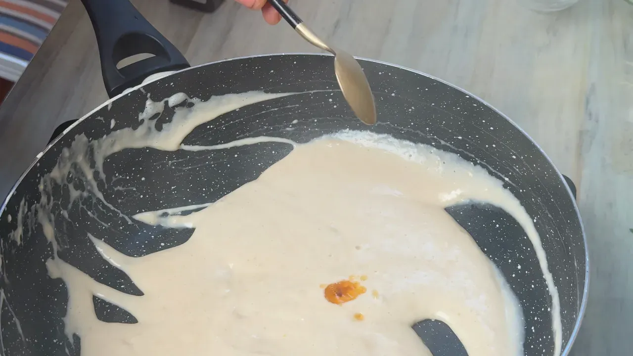 A drop of liquid smoke falling from a spoon into the thickened cheese in the pan
