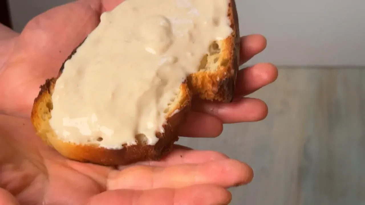 A slice of toasted bread thickly spread with the creamy vegan cheese, held in one hand