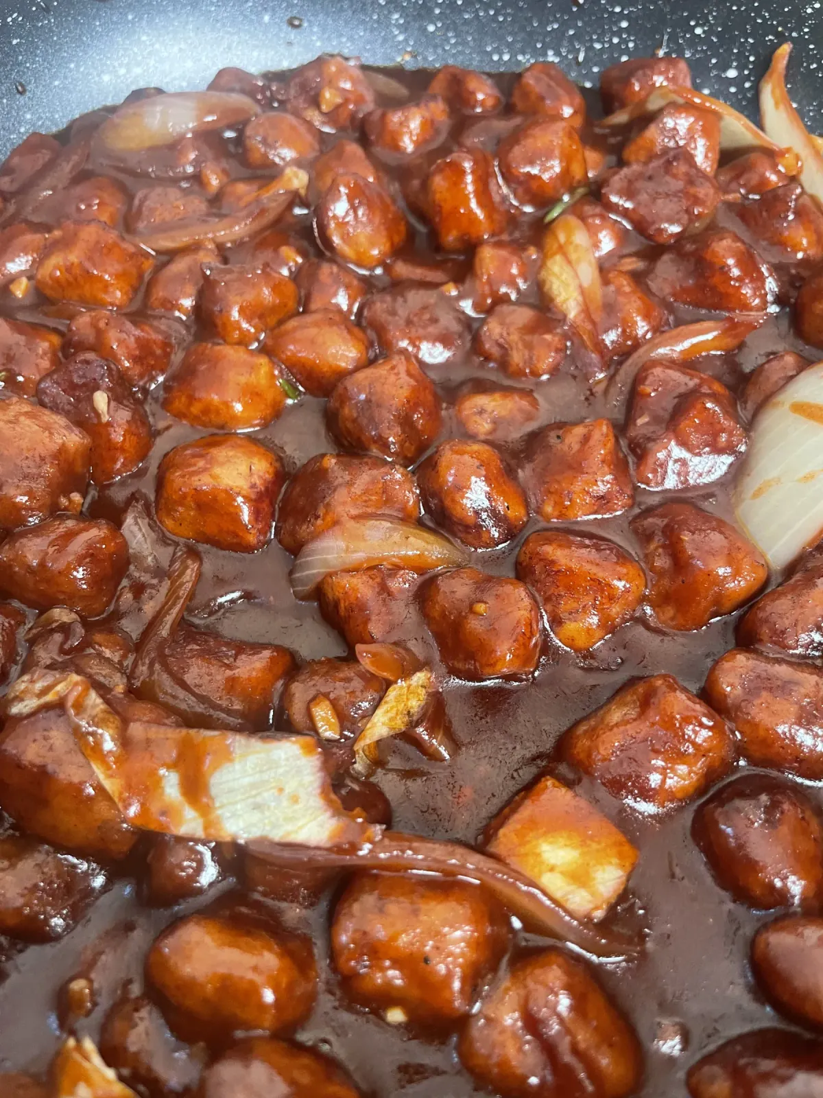 A skillet of glistening dark soy chunks simmered in a sticky chili miso sauce with caramelized onions