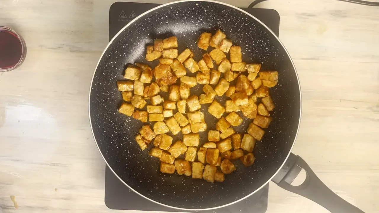 Golden browned tempeh cubes spread out in a black non-stick pan, seen from above
