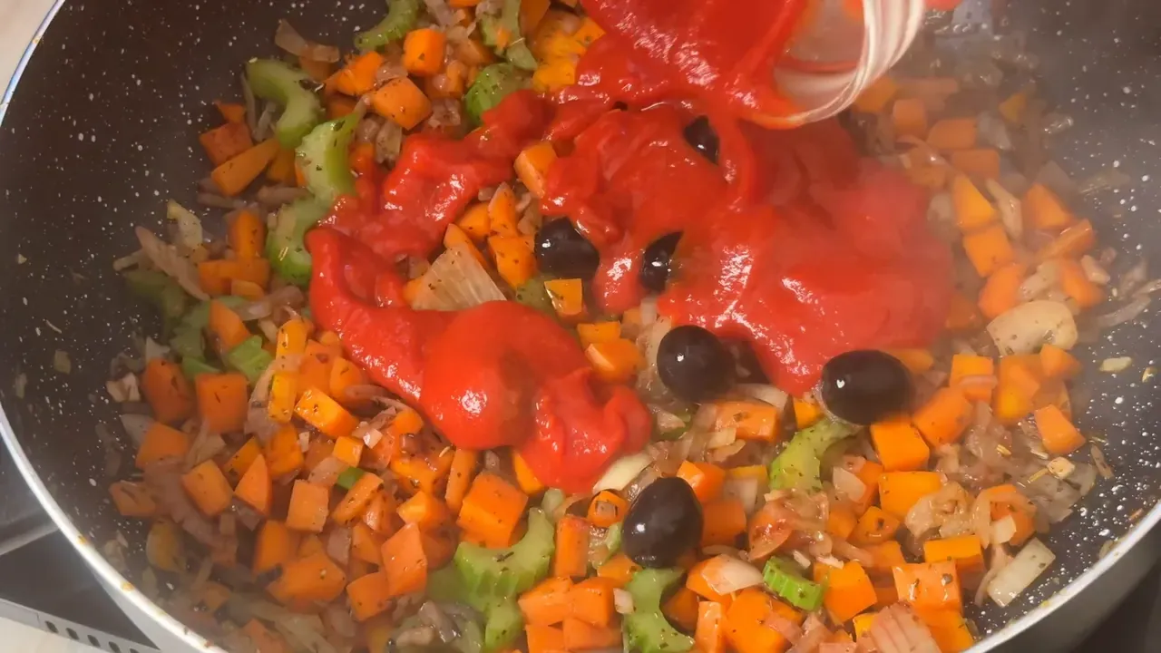 Tomato passata poured over black olives, diced carrot, celery and onion in the pan