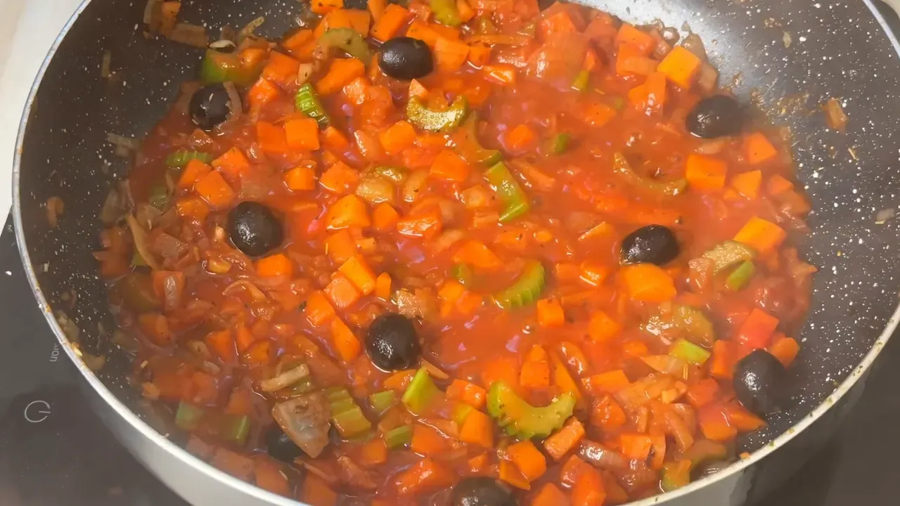 Tomato sauce with diced carrot, celery and whole black olives simmering in the pan
