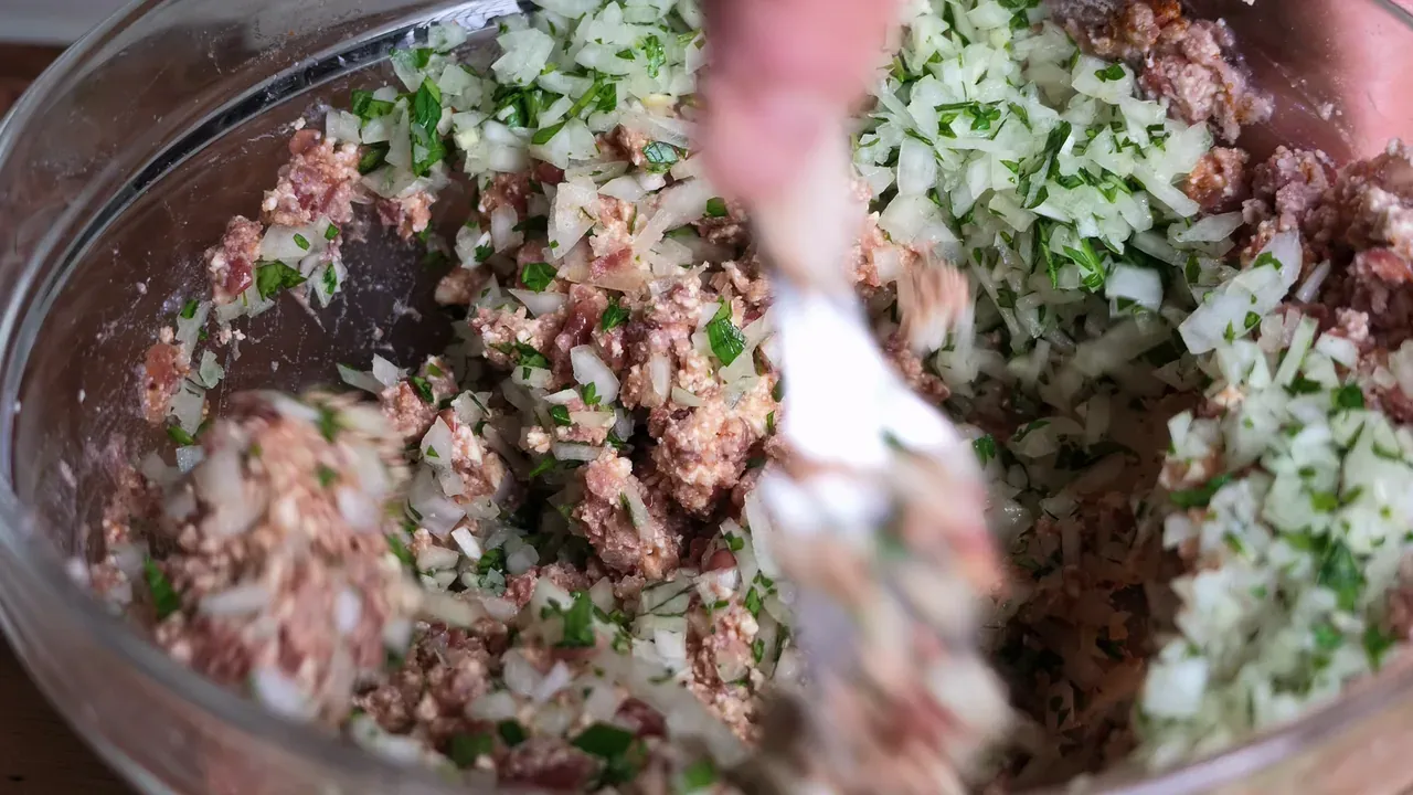 A fork mixing chopped onion, garlic and parsley into the mashed beans and tofu in a glass bowl