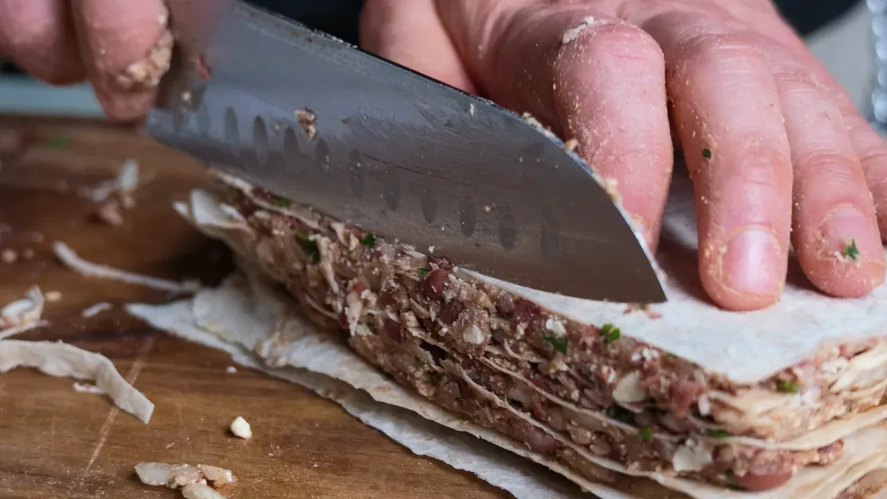 A knife trimming the edge of a stack of tortillas layered with the bean and tofu filling