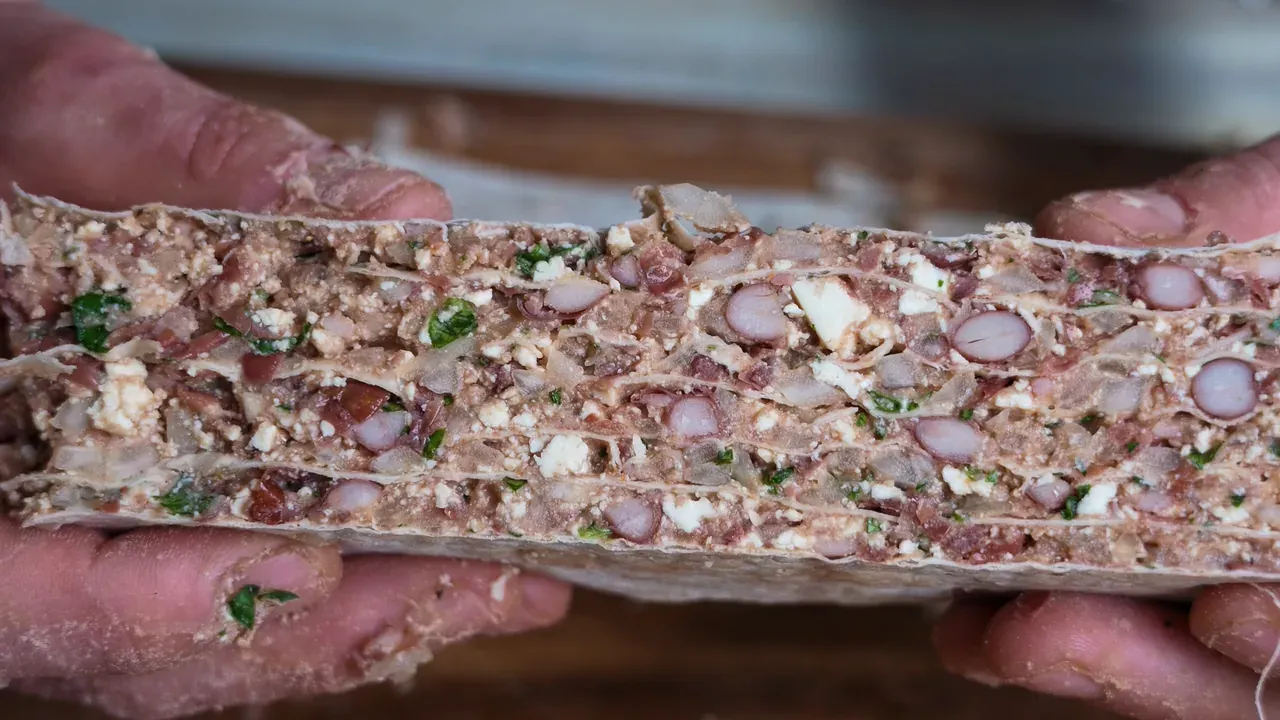 One cut piece of the layered block held up, showing tortilla layers and red beans in cross-section