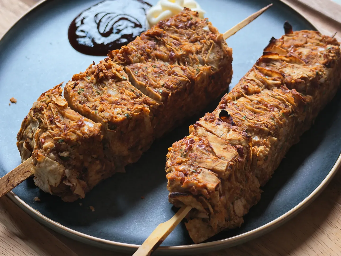 Two baked layered tortilla, bean and tofu skewers on a dark plate with vegan mayonnaise and dark BBQ sauce