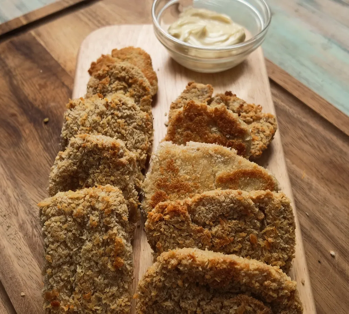 Golden panko-crusted tofu chickpea nuggets in two rows on a wooden board, a small bowl of vegan mayonnaise behind them