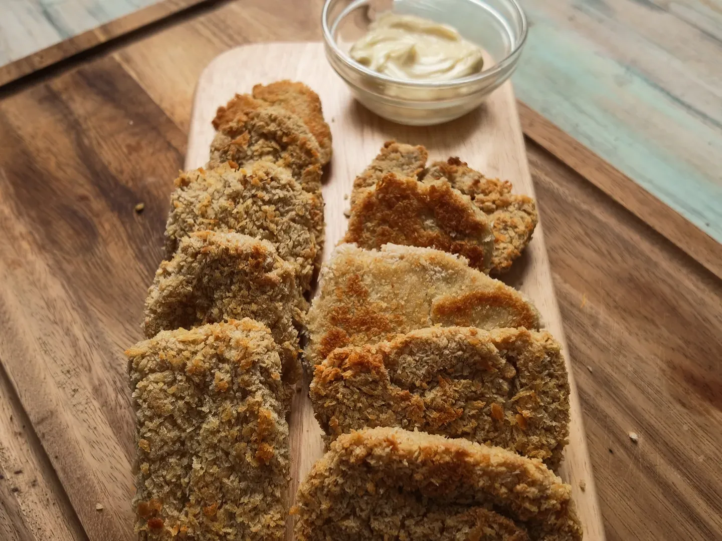 Golden panko-crusted tofu chickpea nuggets in two rows on a wooden board, a small bowl of vegan mayonnaise behind them