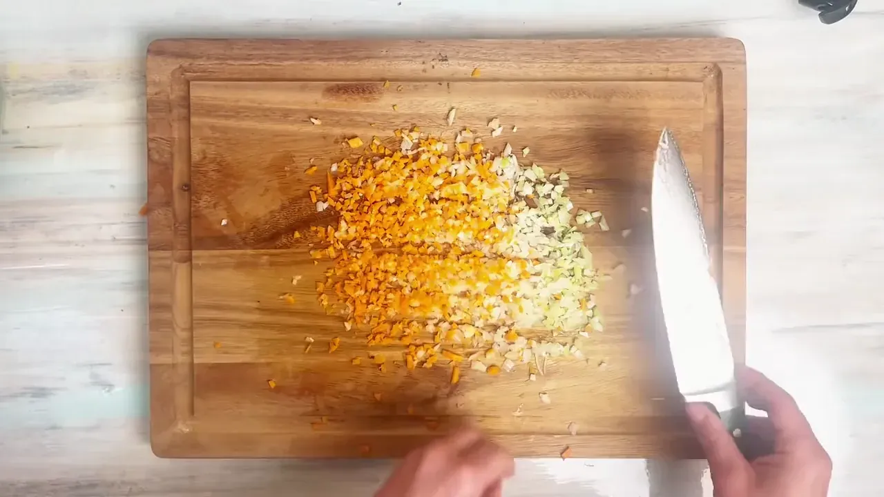 Finely dice the celery stalk, carrot, and onion on a chopping board to create the classic Italian soffritto battuto.