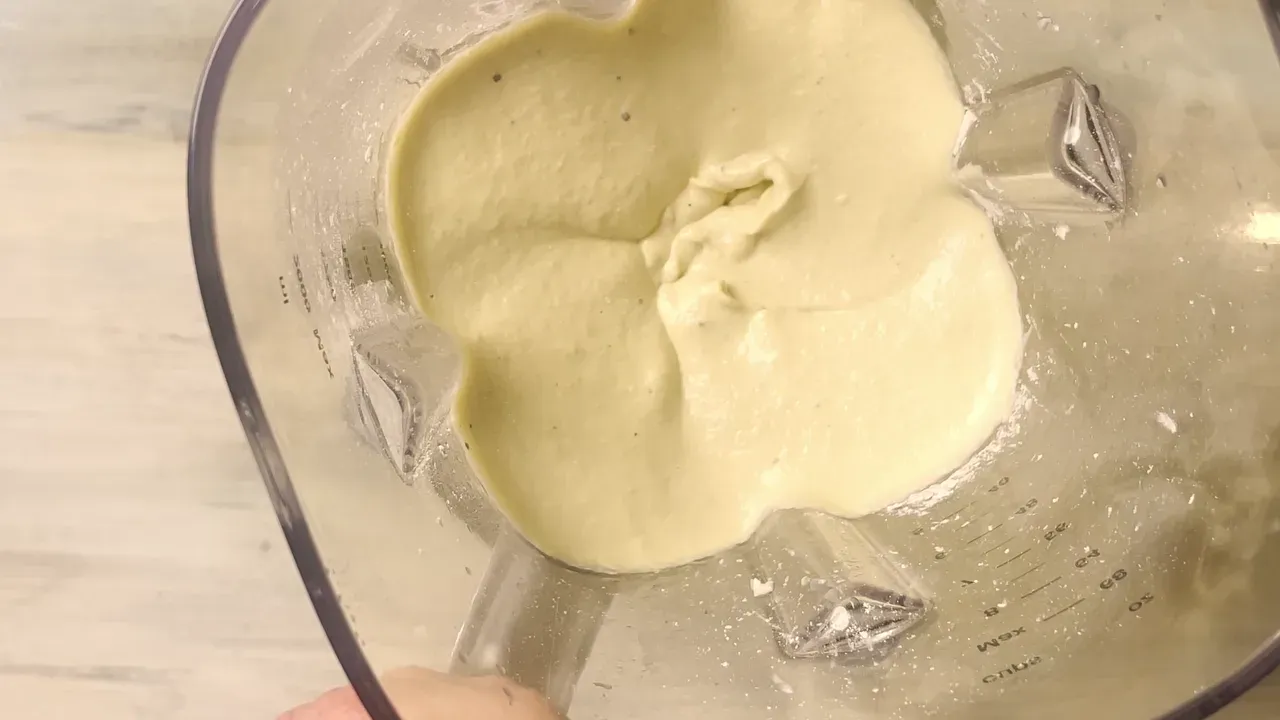 Crema liscia giallo chiaro di anacardi e tofu nel bicchiere del frullatore, vista dall'alto