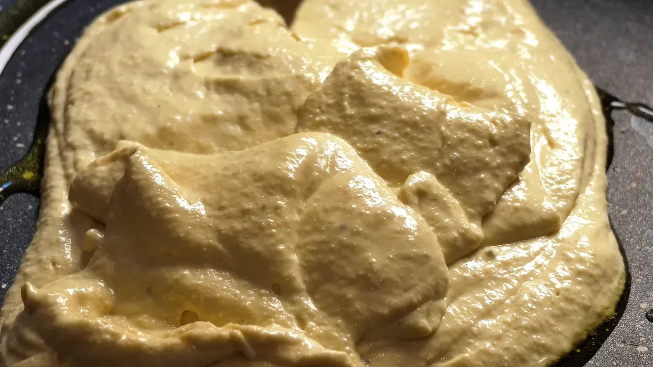 La crema frullata appena versata in una padella antiaderente nera, in primo piano