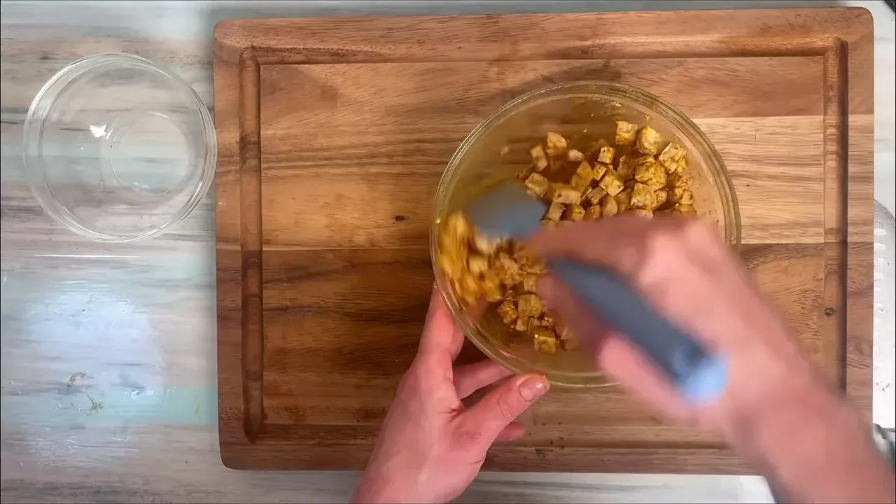In una ciotola mescolo il tempeh a dadini con la salsa di soia, la paprika affumicata, l'olio extravergine, il pepe nero e l'aglio in polvere finché ogni pezzetto è ben marinato.
