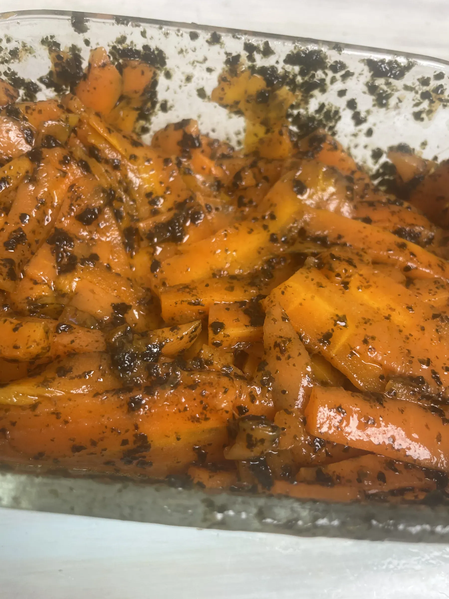 A clear glass dish filled with glossy marinated carrot salmon ribbons seasoned with nori seaweed flakes and sesame oil
