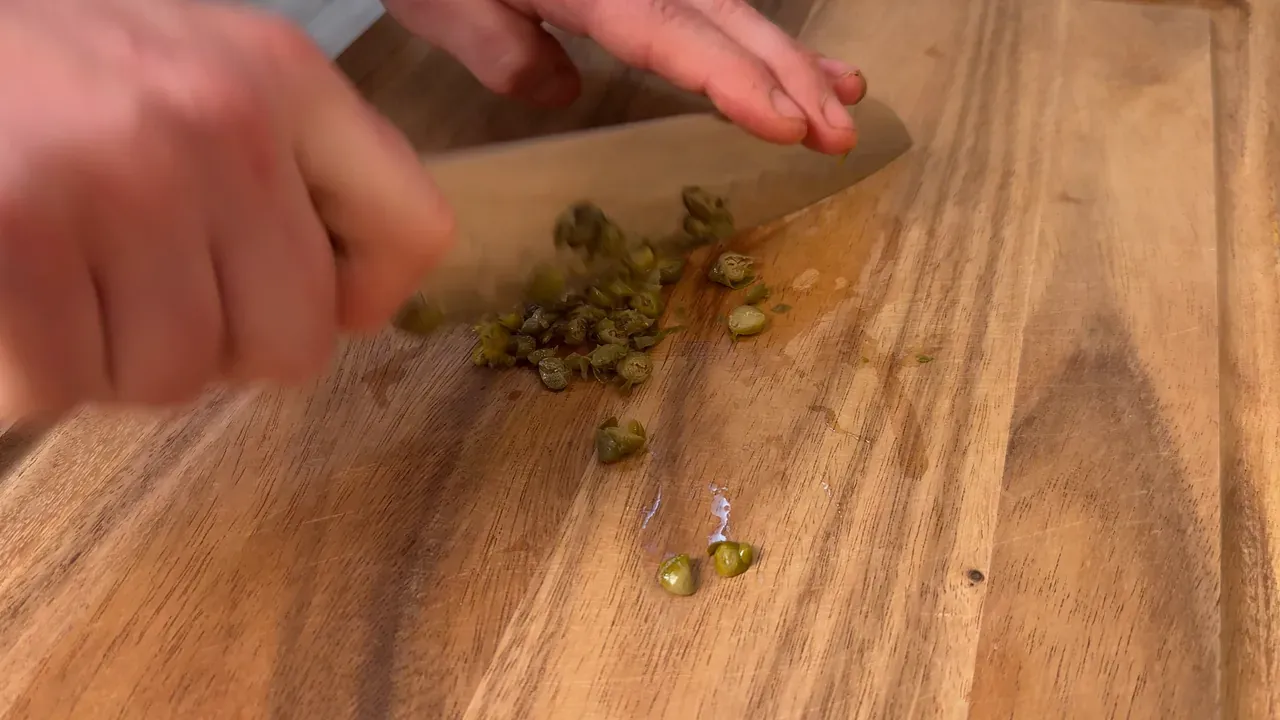A knife chopping capers on a wooden board