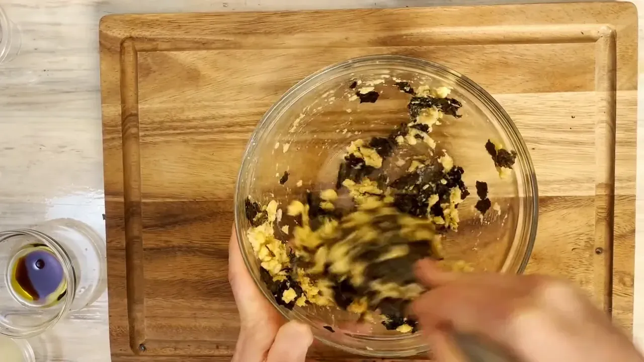 Mashed chickpeas, nori flakes and mustard being whisked together in a glass bowl