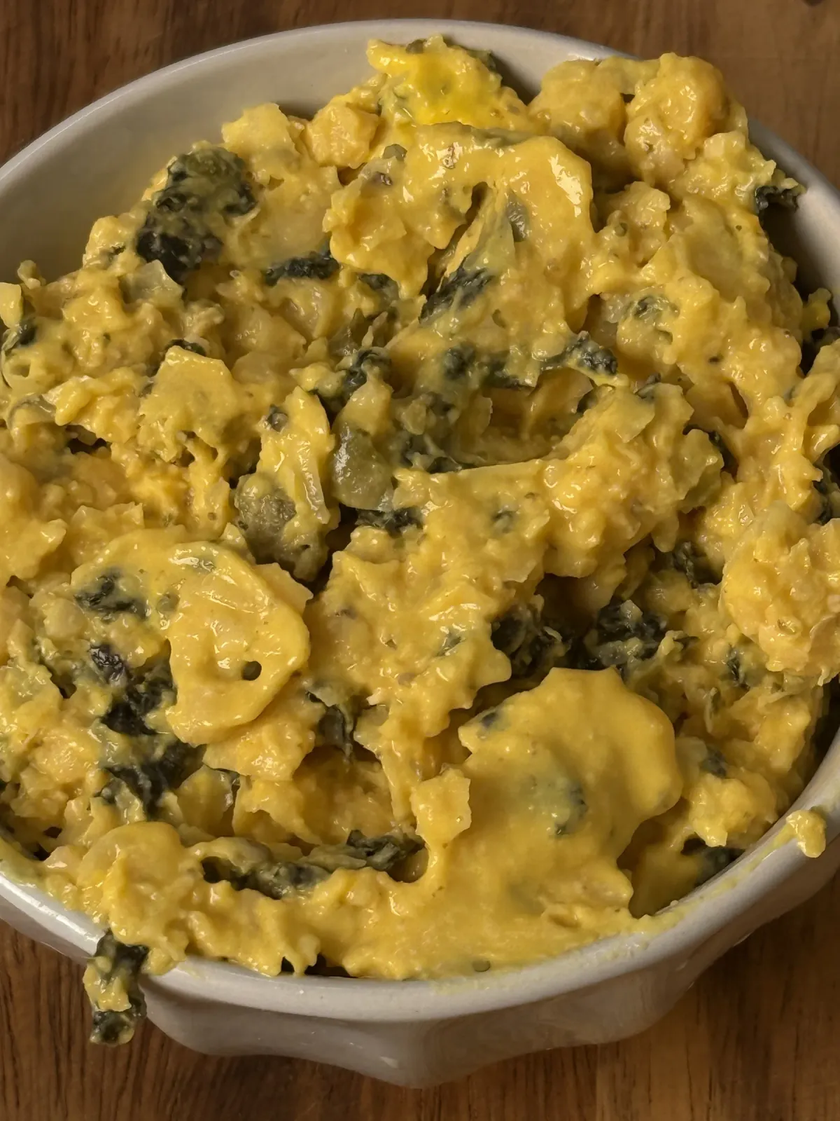Pale ceramic bowl filled with coarse yellow chickpea tuna flecked with dark nori and capers, on a wooden table