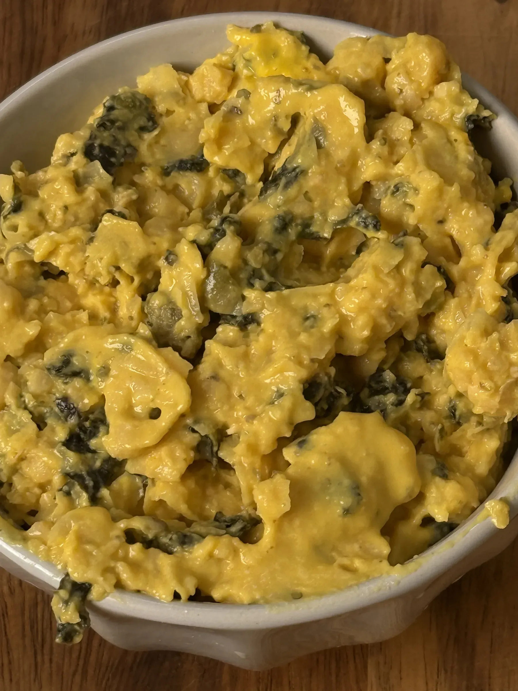 Pale ceramic bowl filled with coarse yellow chickpea tuna flecked with dark nori and capers, on a wooden table