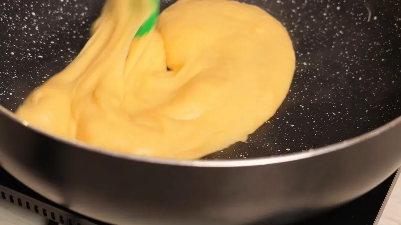 Thick yellow dough being stirred with a green spatula in a non-stick pan