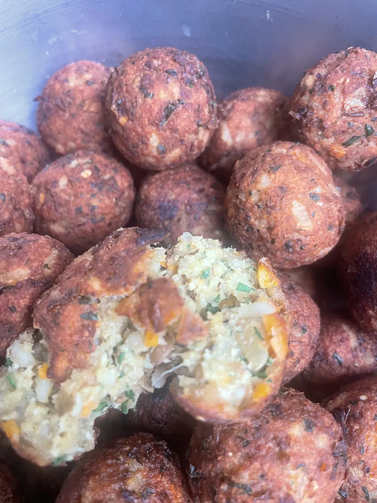 A bowl of golden, crispy fried vegan veggie balls made with lentils and rice, one split open showing the savory interior