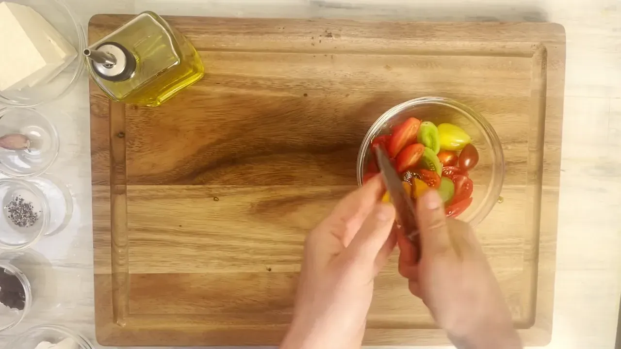 Halve all the cherry tomatoes and place them in a bowl. Peel the garlic clove and crush it flat with the side of your chef's knife blade.