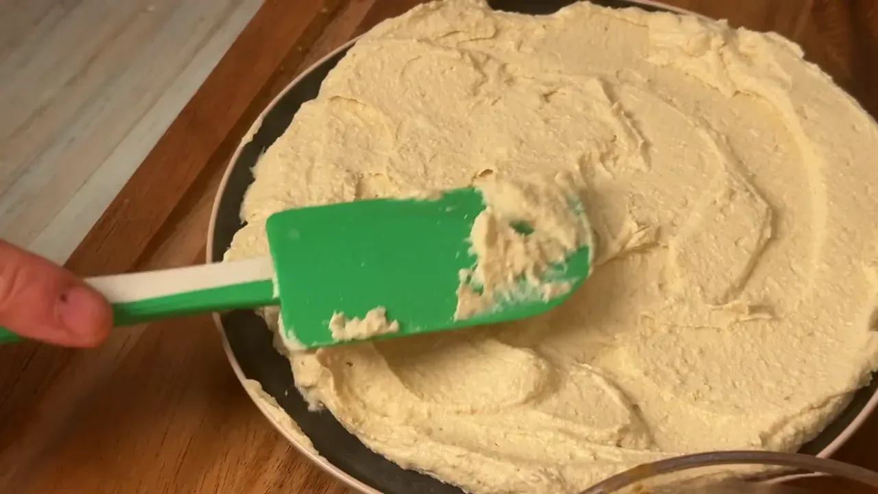 Spread the chilled cream across a serving plate using the back of a spatula or spoon to create a thick, generous bed with gentle swirls and a shallow well in the center.