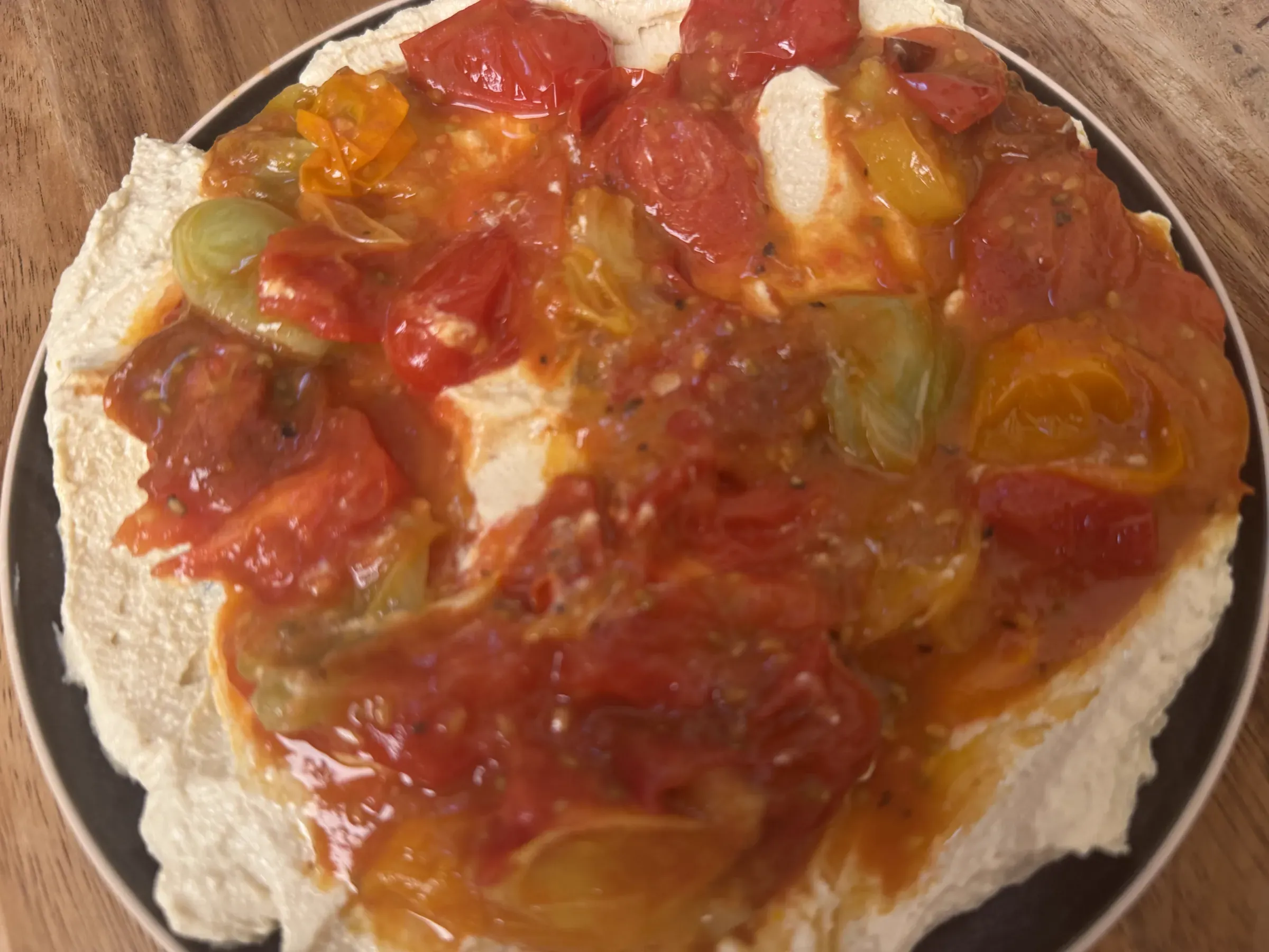 A plate of velvety whipped tofu cream topped with warm blistered cherry tomato confit, rich pan juices, and fresh basil