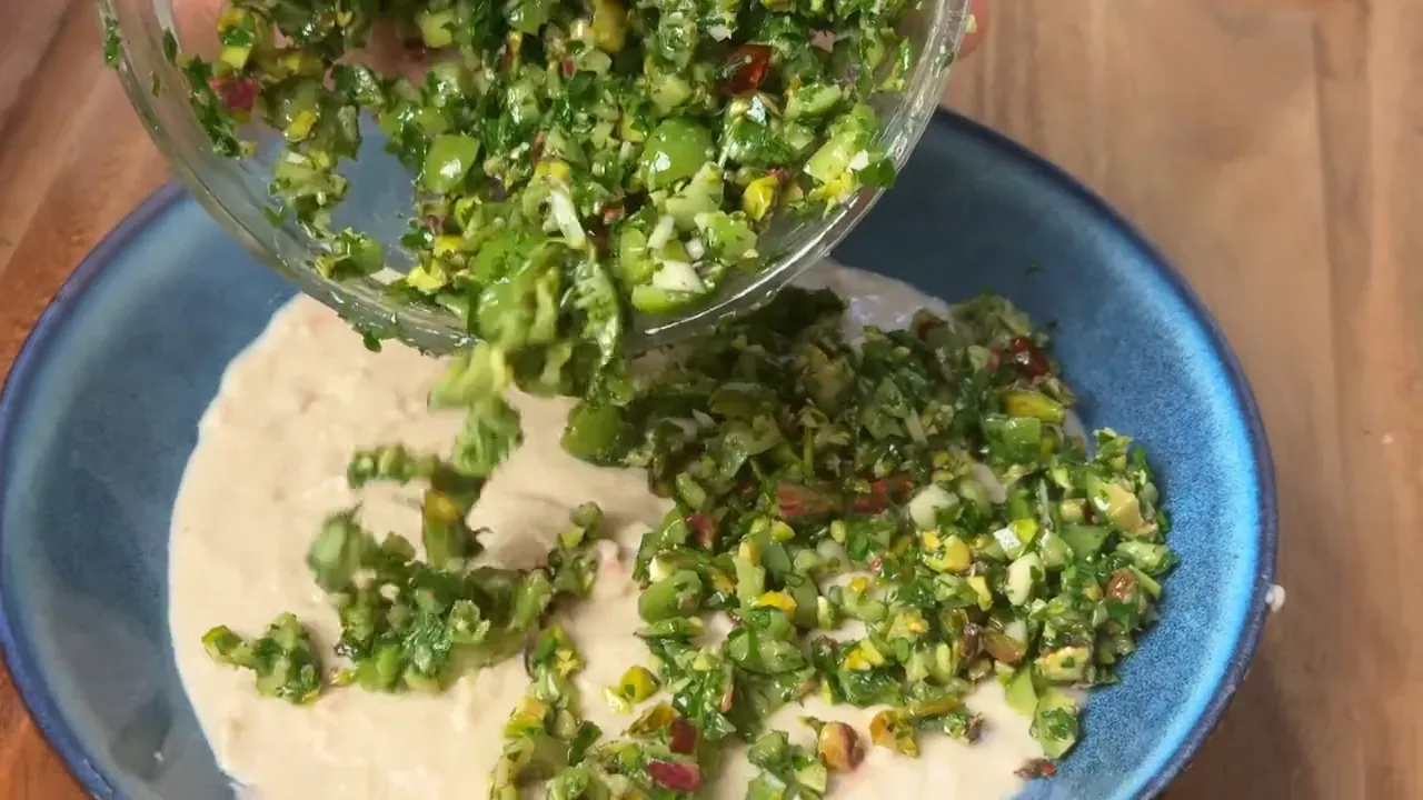 Pistachio salsa verde being tipped from a glass bowl onto the white bean cream